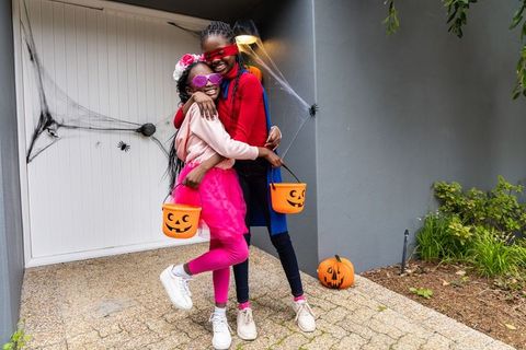 African american sisters celebrating halloween in colorful costumes, hugging on porch