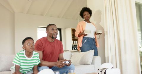 African american family playing video games together while mother serving drinks at home