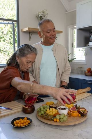 Asian senior couple preparing and arranging fresh fruit platter on kitchen counter