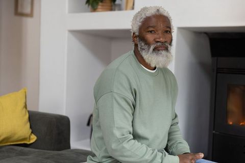 Senior african american man sitting by fireplace in cozy living room in sage sweatshirt