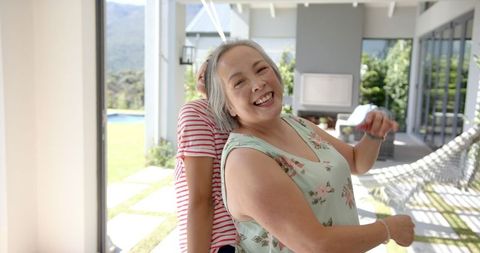 Asian grandmother and granddaughter joyfully dancing at home
