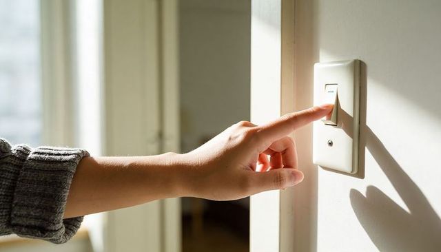 Hand Pressing Light Switch in Sunlit Minimalist Interior with Knit Sleeve Closeup