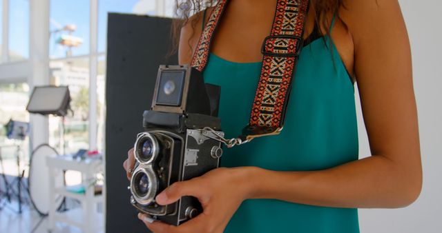 A woman holding a vintage camera in a modern studio. Ideal for use in articles, blogs, or promotions related to professional photography, creative ventures, or the resurgence of film photography.