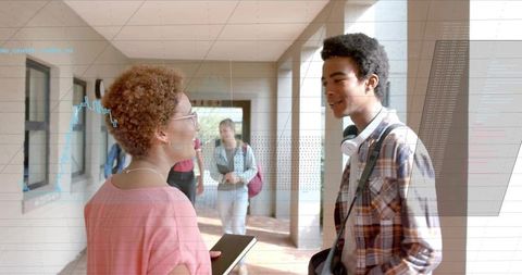College students chatting in sunlit corridor holding tablet and headphones, campus life