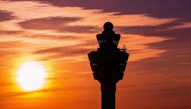 Control tower silhouetting against fiery sunset sky with sun and radar silhouette