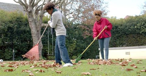 Mother and son raking leaves in autumn garden