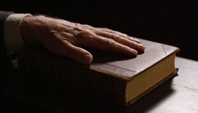 Senior Hand Pressing Antique Leather-Bound Book on Wooden Desk Close-Up