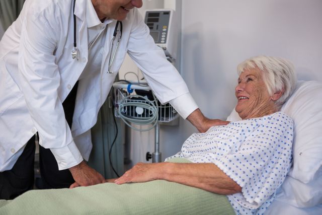 Doctor examining a smiling senior patient in a hospital ward. Ideal for use in healthcare, medical, and senior care-related content. Can be used in articles, brochures, and websites focused on patient care, hospital services, and elderly health.
