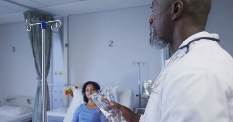 Doctor adjusting iv fluid bag while consulting patient at bedside in hospital ward