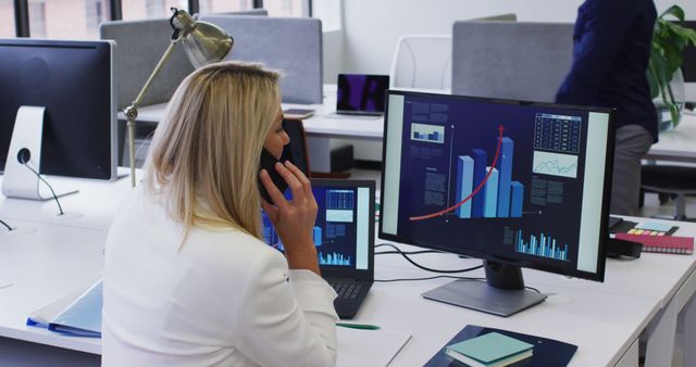 Female professional multitasking in modern office. Uses data chart for analysis and speaks on phone. Suitable for business, technology, work environment contexts.