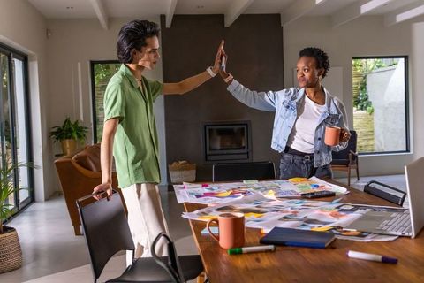 Diverse coworkers high-fiving over sticky-note brainstorming in modern home office
