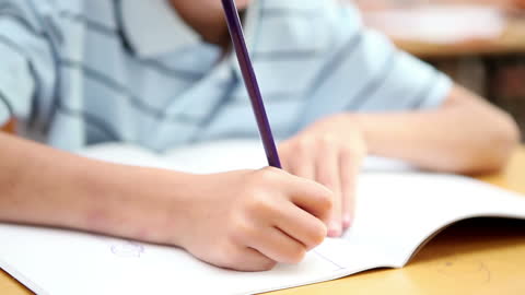 School Child Writing in Classroom Notebook