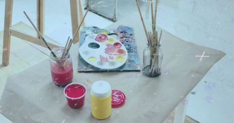 Showing artist workspace with oval paint palette, brush jars and vibrant paint pots