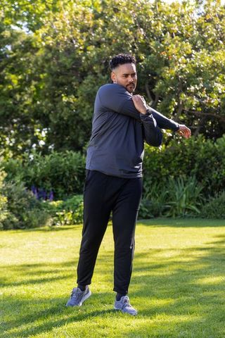African american man stretching in sunlit park wearing activewear and fitness tracker