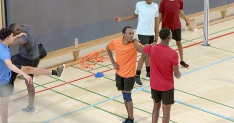 Diverse male teammates standing and talking during indoor agility training on hardwood court