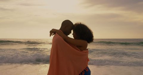 Romantic Couple Embracing on Beach at Sunset Wrapped in Blanket