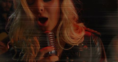 Singing blonde rock vocalist holding retro microphone in moody club close-up