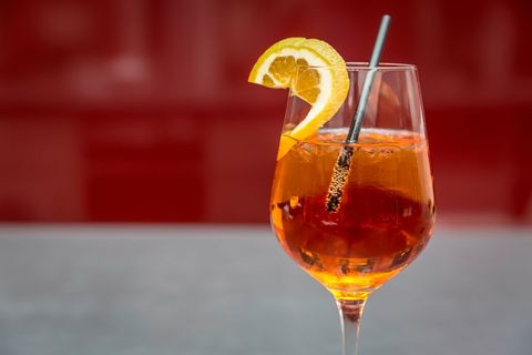 Elegant spritz cocktail garnished with orange slice against red background