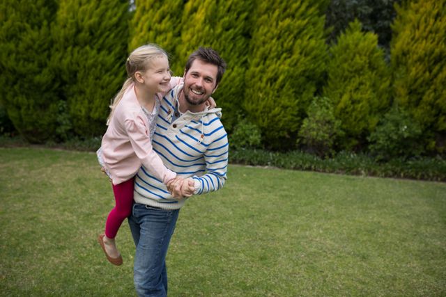 Father and daughter enjoying a playful moment dancing together in a lush green park. Ideal for use in family-oriented advertisements, parenting blogs, and lifestyle magazines. Perfect for illustrating themes of family bonding, joy, and outdoor activities.