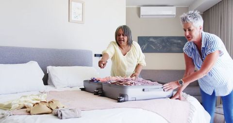 Senior lesbian couple packing suitcase on bed for travel adventure