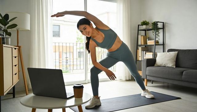 Young woman stretching in modern living room following online fitness workout on laptop