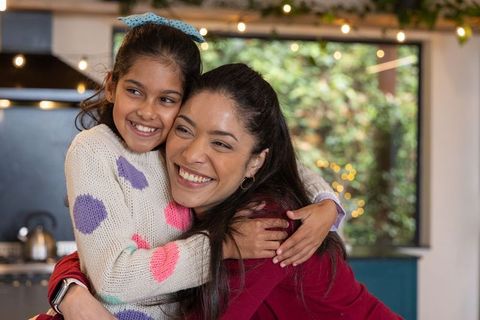 Smiling indian mother hugging daughter in cozy kitchen wearing heart sweater, family bond