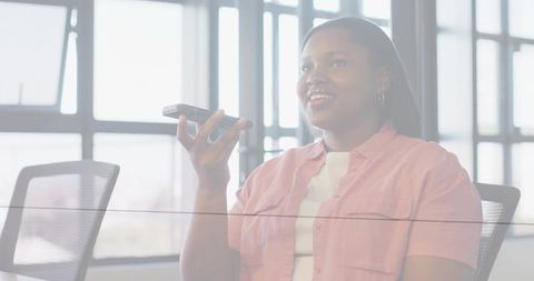Businesswoman speaking into smartphone during office meeting with glass partition