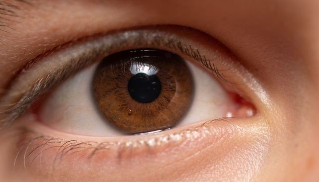 Macro close-up showing brown iris detail, lashes and skin texture with tear reflection
