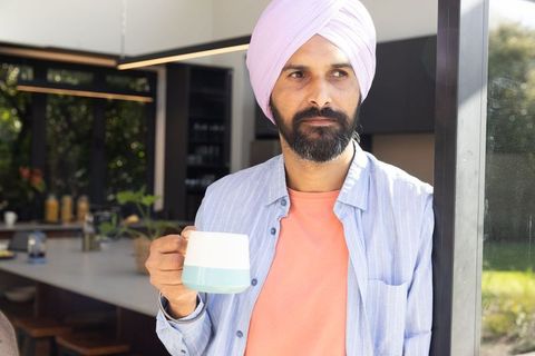 Middle-aged Indian Man Contemplating while Holding Coffee Mug in Modern Kitchen