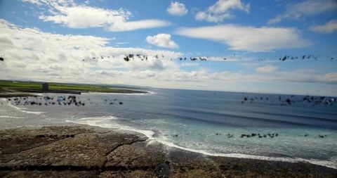 Aerial rocky coastline with historic tower, breaking surf and blue cloudy sky panorama