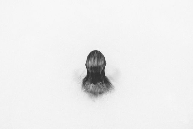 A person with medium length hair seen submerged in water, creating a minimalist and peaceful effect. Ideal for use in themes related to relaxation, solitude, mental health, and simplicity. Can be used in advertisements, social media, blogs, and wellness articles to invoke a sense of calm and peace.