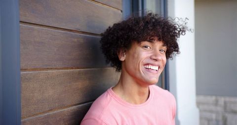 Joyful young man leaning on wooden wall in casual wear