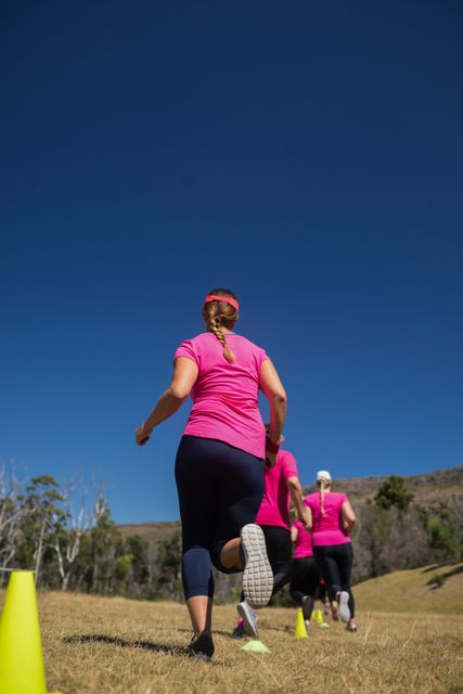 Group of women participating in a boot camp, running through cones on a sunny day. Ideal for promoting fitness, teamwork, and outdoor activities. Useful for advertisements, fitness programs, and health-related content.