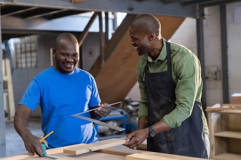 African american craftsmen collaborating on woodworking project in industrial workshop