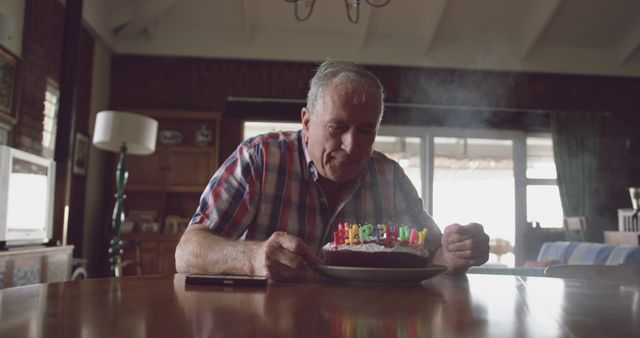 Caucasian senior man blowing candles on birthday cake at home. Retirement, senior lifestyle, happiness, domestic life, birthday, celebration and wine making, unaltered.