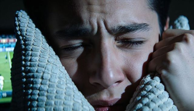Anxious teen pressing into chunky knit blanket under blue tv light, gripping fabric