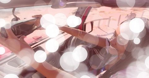 Young woman with sunglasses adjusting rearview mirror in vibrant sunlit car