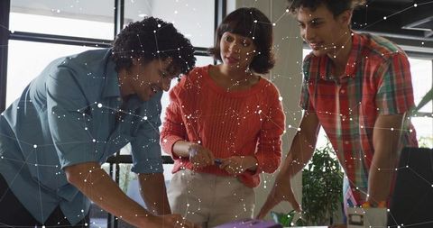 Colleagues collaborating and leaning over desk, analyzing plans with digital network overlay