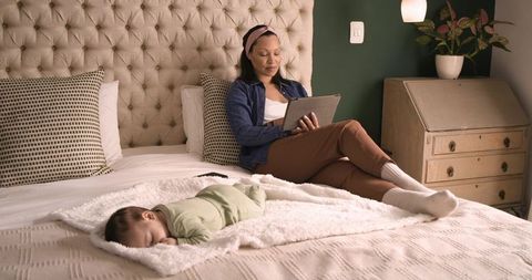 Mother Reading on Tablet as Baby Sleeps Peacefully in Cozy Bedroom