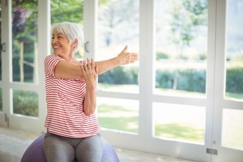 Senior Woman Stretching on Exercise Ball in Bright Home Gym