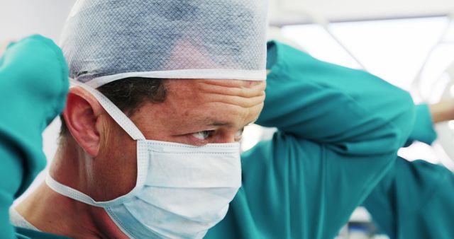 A surgeon focusing while adjusting medical cap and mask inside an operation room. Ideal for use in healthcare articles, medical journals, hospital promotional materials, or educational posters related to medical professions and surgery.