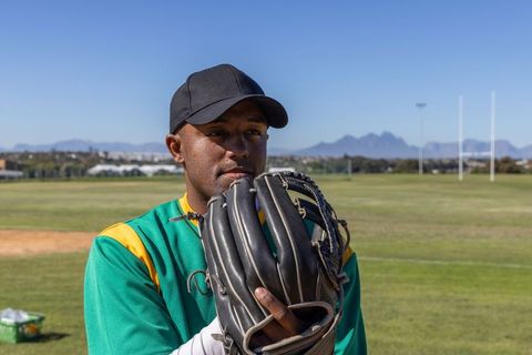 African american baseball player holding mitt near face on sunny field with mountains