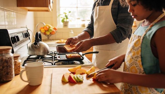 Parent and child cooking together: slicing fruit and toasting sandwich on stovetop