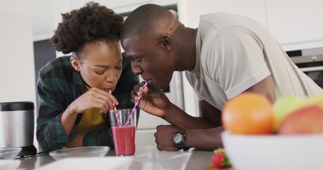 African American couple sharing a smoothie in a modern kitchen, highlighting themes of love, bonding, and healthy lifestyle. Useful for articles or promotions related to healthy living, relationship tips, and modern home layouts.