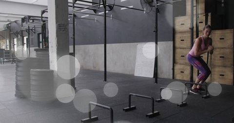 Woman performing box squat with parallettes in industrial crossfit gym, fitness training