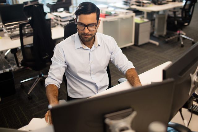 Young businessman working at his desk in a modern office environment. Ideal for use in business, technology, and corporate productivity themes. Suitable for illustrating professional work settings, employee engagement, and modern office culture.