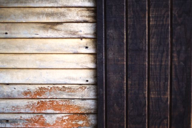 This image depicts a close-up view of an old wooden wall with a combination of light and dark brown rustic textures. The weathered appearance on one side contrasts with the smoother, darker wooden panels on the other, creating a unique and appealing abstract design. Perfect for use in backgrounds, design projects, architecture themes, and vintage decor concepts.