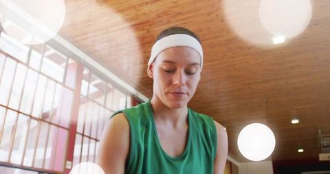 Female athlete in green jersey and white headband focusing during indoor court training