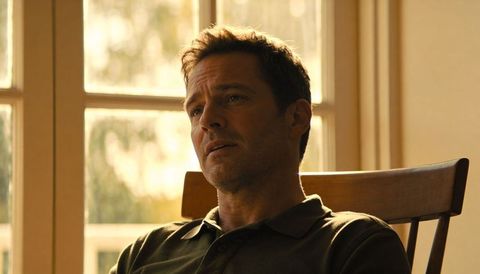 Contemplative man sitting in slat-back chair by sunlit window, warm backlit interior light