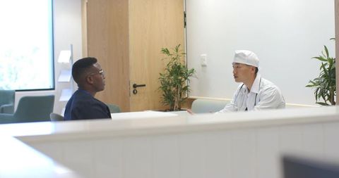 Asian physician consulting with african american patient at modern clinic reception area